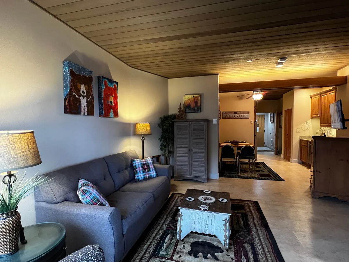 A cozy living area featuring a plush sofa, stylish artwork, a coffee table, and a warm lamp, creating an inviting atmosphere ideal for relaxation. The decor hints at a comfortable retreat where guests can unwind after a day of adventure.