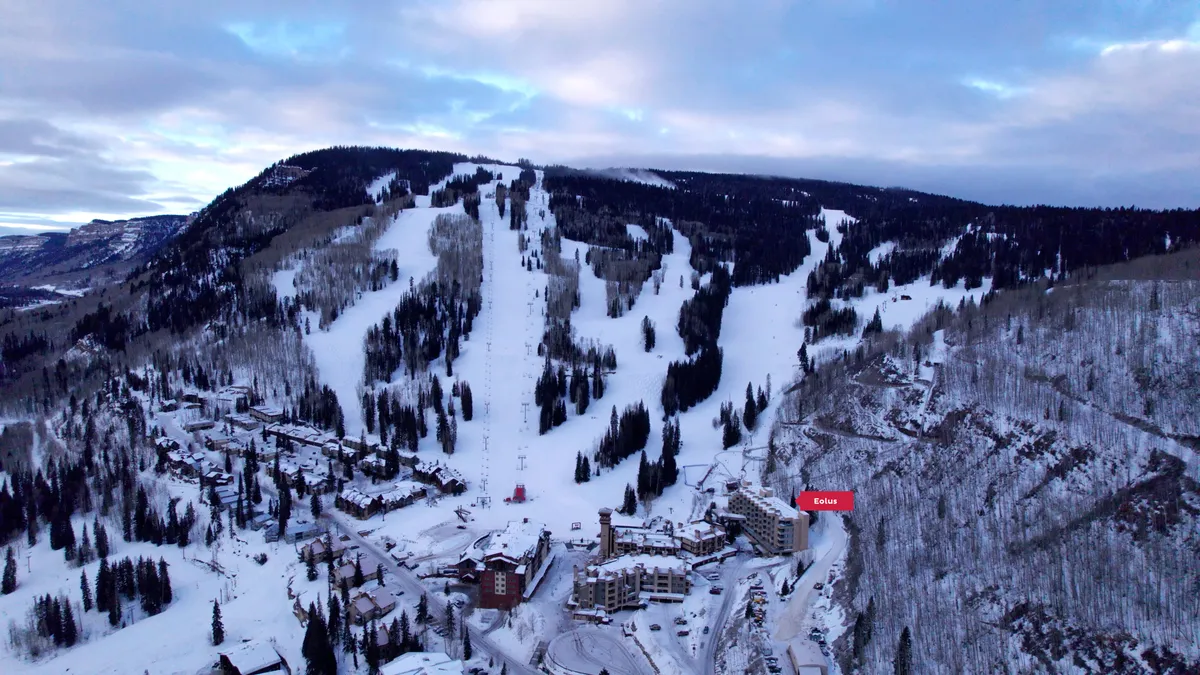 A sweeping exterior view of ski slopes framed by snow-laden trees and nearby residential buildings. The image evokes the tranquil beauty of the mountain setting and shows the close proximity of accommodations to the ski area.