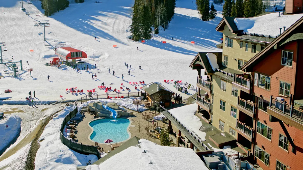 An exterior view of the resort with a swimming pool in the foreground, ski slopes, a ski lift, outdoor seating, and lodging buildings. The scene captures the excitement of outdoor activities alongside relaxation spaces, set against a snowy mountain backdrop.