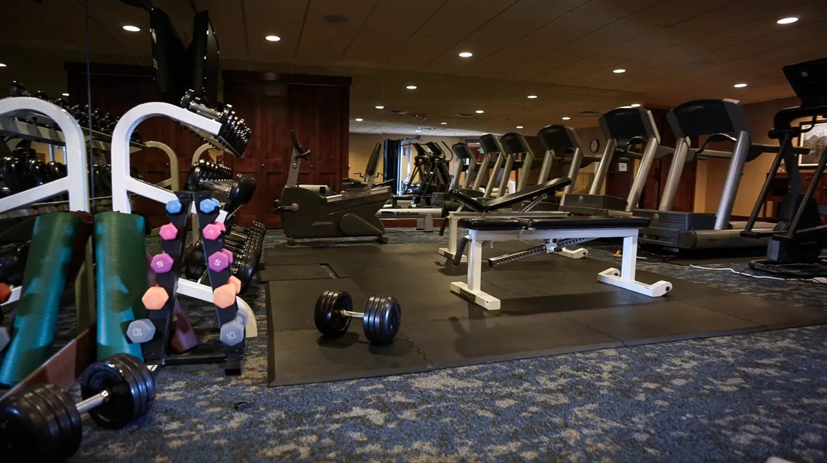 This image showcases an on-site fitness facility equipped with dumbbells, treadmills, an exercise bench, and other strength training equipment. The setting is bright and modern, offering a motivational atmosphere for guests to maintain or kickstart their workout routines.