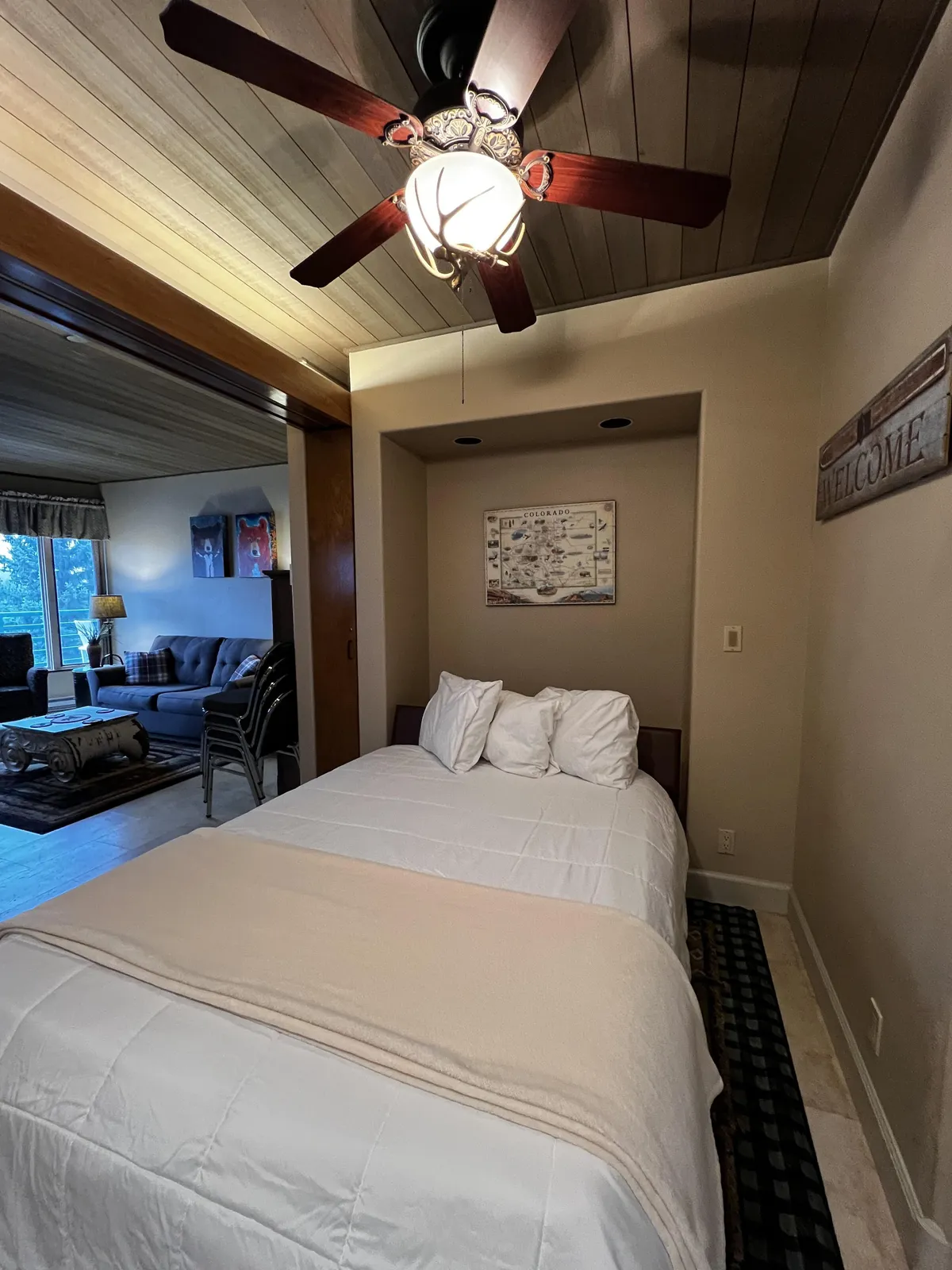 A cozy bedroom area with a bed, ceiling fan, decorative wall art, and a couch in the background. The room's layout suggests flexibility for both rest and socializing, supporting multi-use living—a key feature for maximizing space in a vacation property.