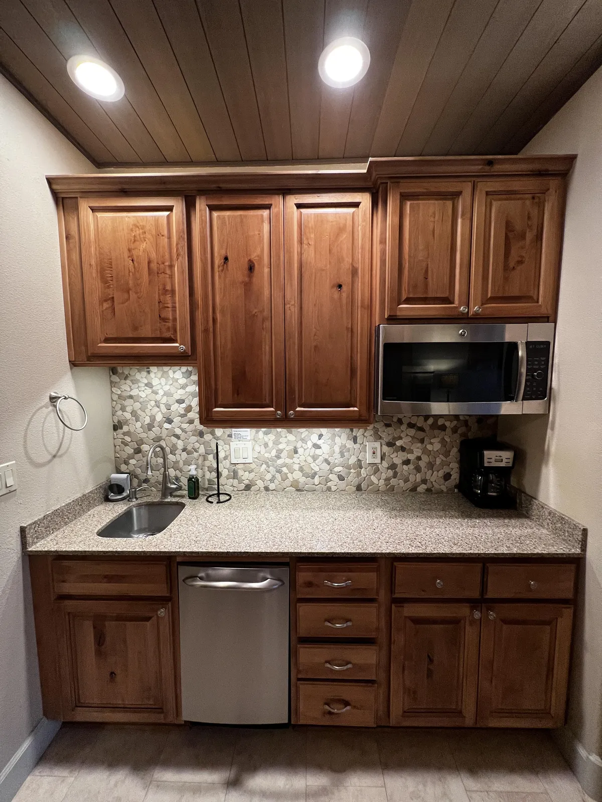 A detailed view of the kitchenette with modern wooden cabinets, granite countertops, decorative backsplash, and up-to-date appliances. The setup is tailored for easy meal prep, perfect for quick breakfasts or romantic dinners.