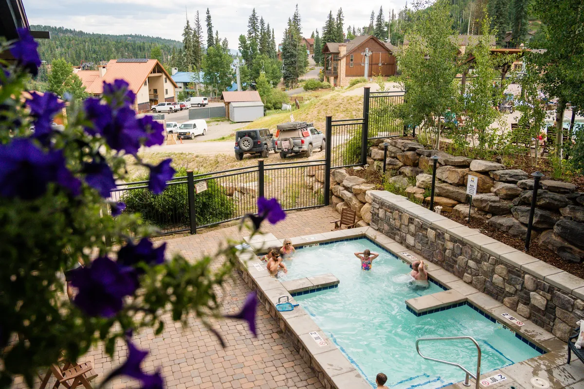 An inviting outdoor hot tub set against a backdrop of natural beauty and mountain views, with flowering plants and serene surroundings. The setting suggests relaxation, socializing, and unwinding after a day of mountain activities.