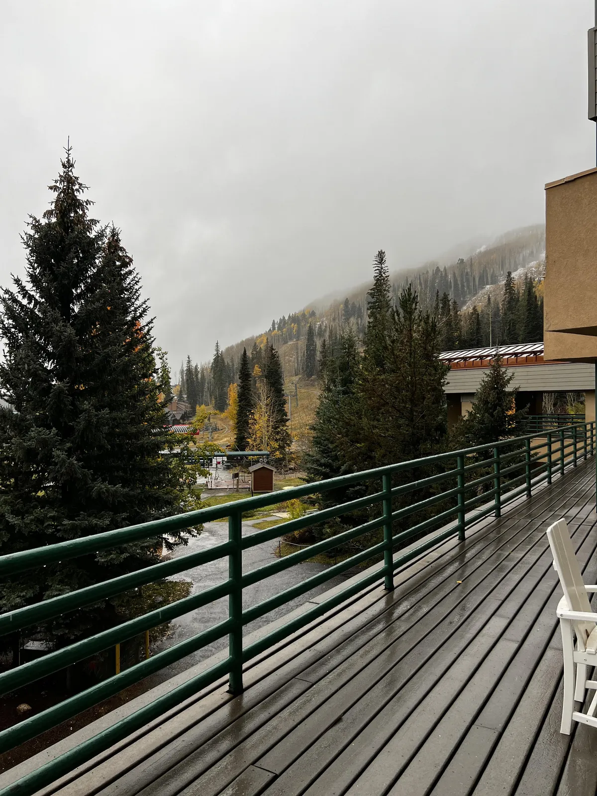 A serene exterior view from the private wooden deck, featuring a single chair overlooking evergreen trees and distant mountains. The deck's railing frames a tranquil space perfect for taking in the fresh air and stunning vistas.